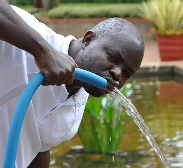 Person drinking clean water from a hose, illustrating the importance of safe drinking water in emergency situations and disaster recovery.