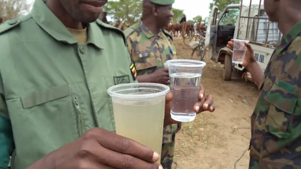 Military personnel holding cups of purified and contaminated water, showcasing the effectiveness of BlueBox mobile water purification systems in field operations